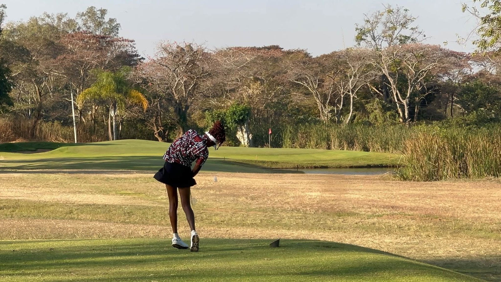 A golfer drives from the tee across an open fairway