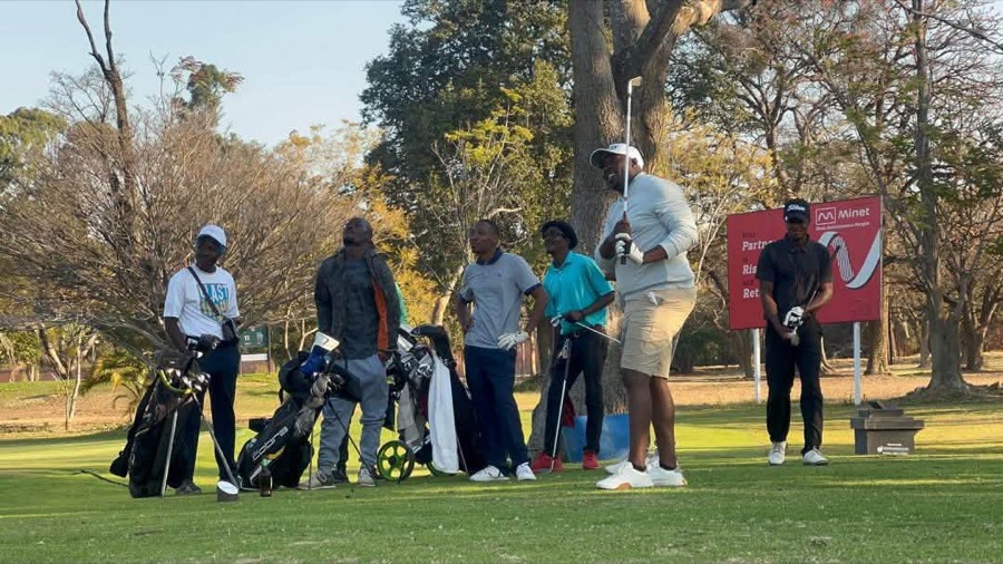 A golfer plays a shot, with a buggy out on the course